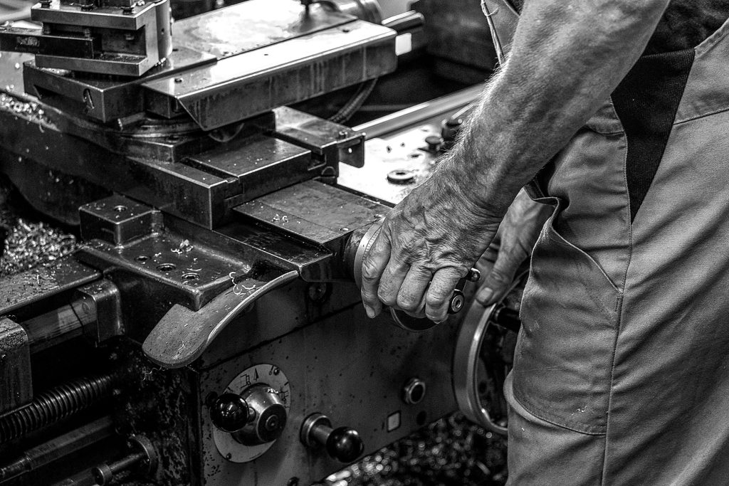 Nahaufnahme einer Hand, die eine Drehmaschine in einer Werkstatt bedient.