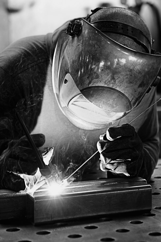 Schweisser mit Schutzhelm und Handschuhen arbeitet konzentriert an einem Metallstück, Funken sprühen.